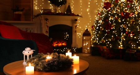 Coffee table with burning candles, fireplace, Christmas tree and festive decor in dark room, selective focus. Interior design