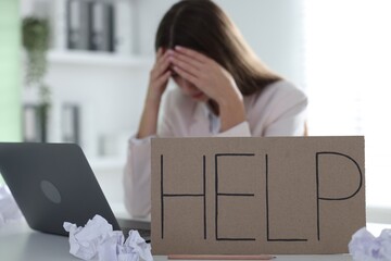 Woman with laptop and sign Help at table in office, selective focus