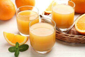 Fresh orange juice, mint and fruits on light wooden table, closeup