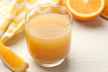 Fresh orange juice in glass and fruits on light wooden table, closeup
