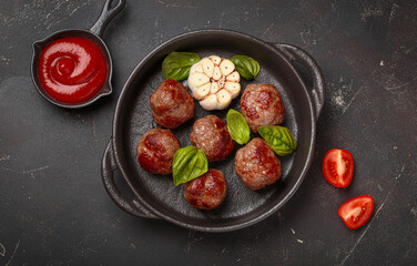 Delicious fried meatballs with basil, garlic in cast iron pan and tomato sauce top view