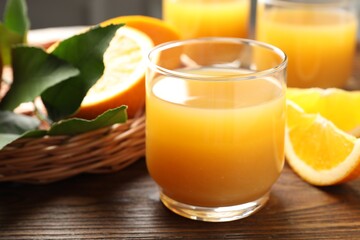 Fresh orange juice, fruits and green leaves on wooden table, closeup