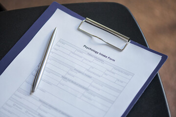 Psychology intake form resting on clipboard with metallic pen placed diagonally, document containing blank fields for patient information and assessment during group therapy session