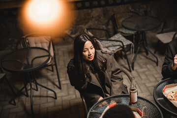 Group enjoys evening gathering at outdoor cafe with drinks and pizza on cozy night in urban setting