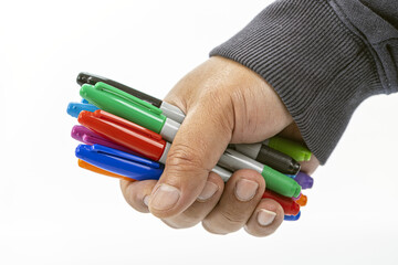 Close-up of a hand tightly holding a collection of colorful permanent markers with various caps visible on a white background