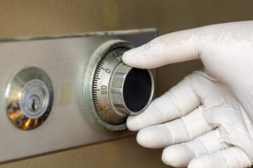 Close-up of a gloved hand carefully turning the combination dial on a metal safe lock to ensure security and protection