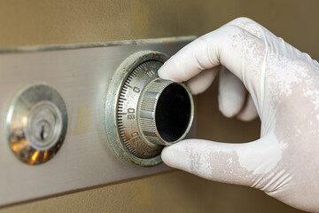 Gloved hand adjusting the dial on an old combination safe lock with visible wear on metal and beige safe body
