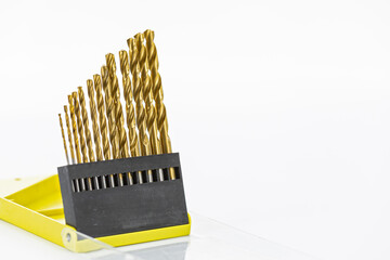 Set of gold-colored drill bits arranged in ascending size order in a yellow plastic case on a white background showing precision
