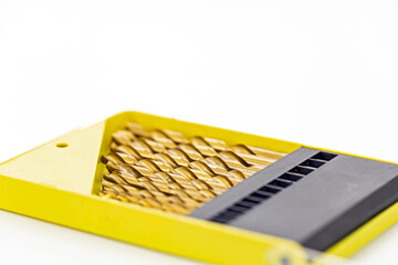 Set of gold metal drill bits arranged neatly in a bright yellow plastic case with a black organizer section on a white background