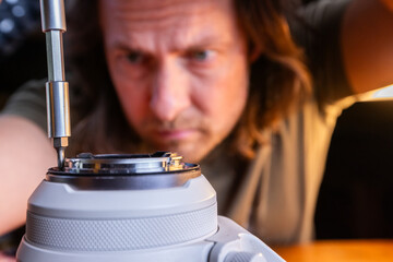 close up of a screwdriver loosening the screws on the rear element of a camera lens and a man...