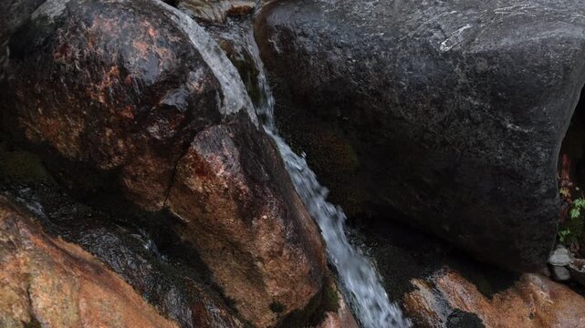 ripresa video frontale e dettagliata, in tempo reale, di un flusso leggero d'acqua che scorre lentamente lungo le pareti rocciose e scure di una cascata di montagna