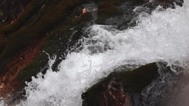 ripresa video laterale e dettagliata, in tempo reale, dell'acqua che scorre impetuoso lungo le pareti rocciose di una cascata di montagna