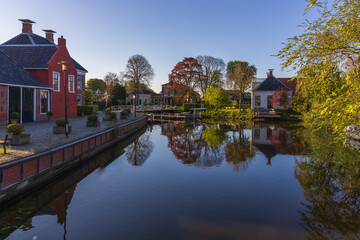 Fototapeta premium A picturesque view of Bedum center in the Netherlands. A calm canal reflects red and white houses, a bridge, and trees. The shot captures a morning spring atmosphere