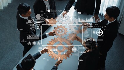 A diverse team of professionals collaborates over a table, utilizing digital displays and gear symbols to visualize strategic planning and innovative approaches in business. Raster
