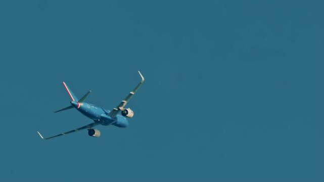 A small aircraft flying across a clear blue sky, captured mid turn with its landing gear visible
