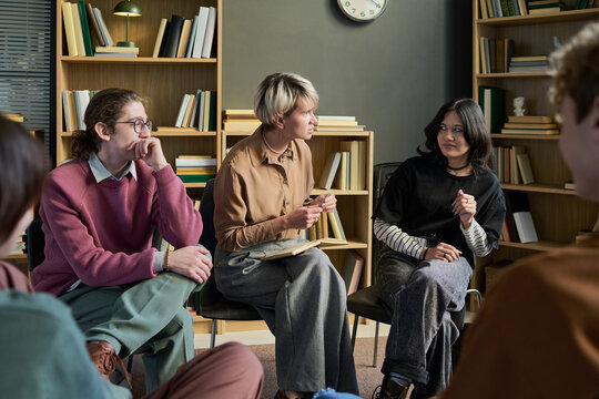 Diverse group of young people and adult women sitting in circle participating in group therapy session, in conversation and sharing experiences in professional setting - Powered by Adobe