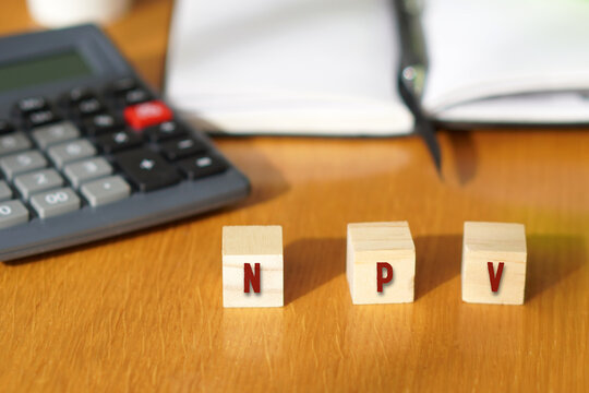 NPV. Business and financial concepts. Letters written on wooden cubes with a calculator and notebook in the background.
