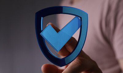 Close-up of a hand holding a digital shield with a checkmark symbol representing security, protection, and approval. Ideal for cybers
