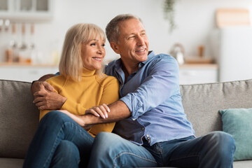 Obraz premium A smiling couple sits closely together on a comfortable sofa in their warm living room, enjoying each other's company and sharing a tender moment.
