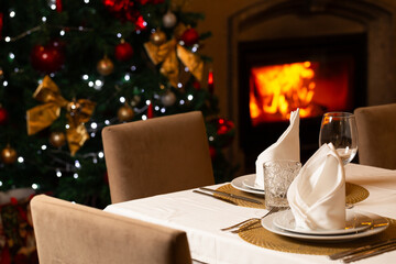 Cozy Christmas dining room with a decorated tree, warm fireplace, festive lights, and an elegant table setting ready for a holiday celebration.