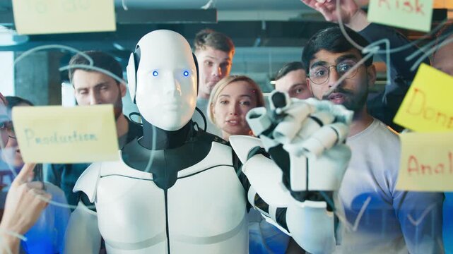 Humanoid robot drawing connections on glass. Group watching closely while planning workflow. Machine marking lines between sticky notes. In active office with team observing behind.