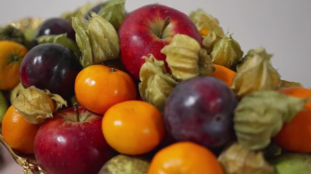 Luxurious fruit centerpiece with mixed apples, glossy plums, golden physalis and vivid citrus, styled for banquet and hospitality shoot, soft directional light