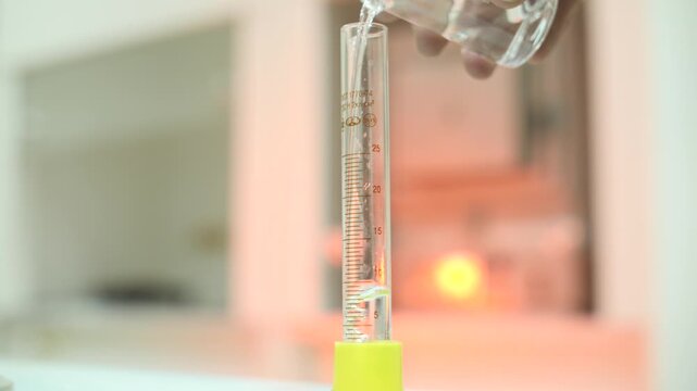 Scientist pouring liquid into graduated cylinder for experiment in lab.