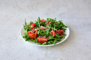 Fresh Arugula and Tomato Salad with Seeds on a White Plate on concrete background
