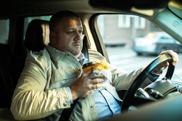 Adult man eating fast food while driving in car, tired