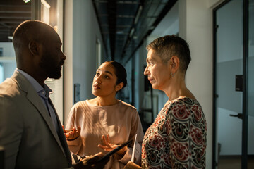 Adult and mature coworkers in focused discussion in office corridor