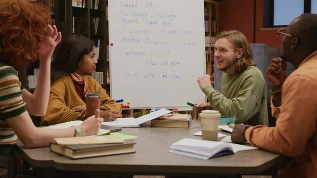 Positive young male teacher introducing basic French phrases written on whiteboard to multicultural group of adult students during beginner class in library