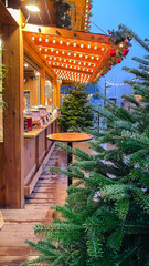Cozy wooden stall at a European Christmas market on a wet evening, with festive lights and pine trees