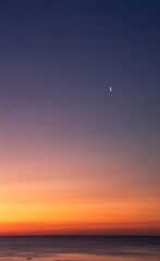 Serene Crescent Moon in a Dramatic Twilight Sky Above a Calm Ocean Horizon