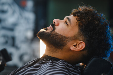 Man getting beard groomed in barbershop chair