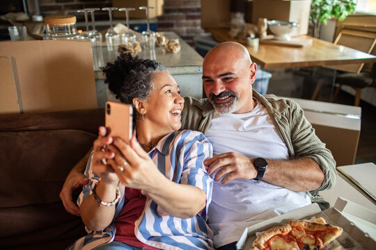 Mature couple laughing, taking selfie in new home living room - Powered by Adobe