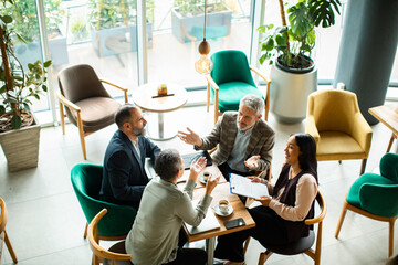 Adult woman and mature men brainstorming at a modern cafe, smiling