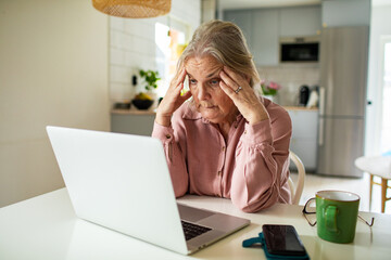 Senior woman feeling stressed working on laptop at home