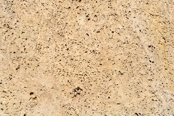A close-up, horizontal full-frame background of a light beige, rough porous stone surface characterized by numerous small, dark holes