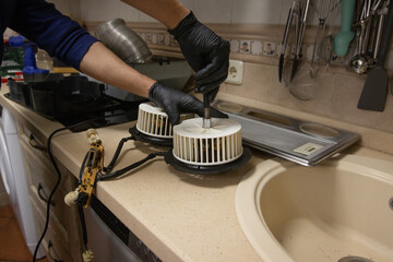 Technician testing extractor fan motors on a kitchen counter during appliance repair. DIY home maintenance, electrical troubleshooting, and ventilation service.