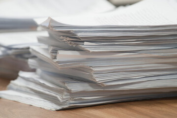Large stack of paper documents piled up on a wooden office desk. Concept of bureaucracy and heavy administrative workload. Photo.