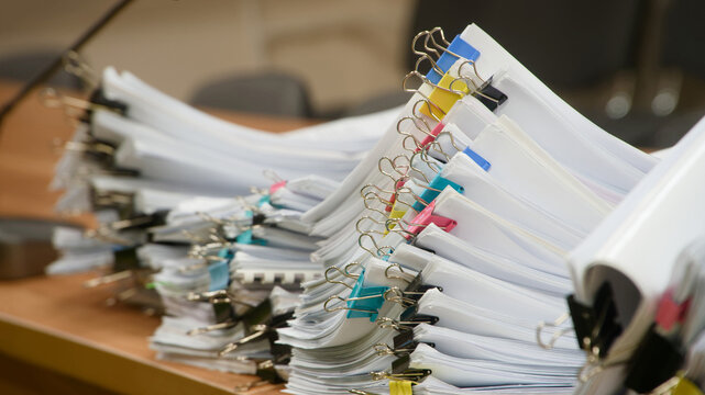 Huge stacks of sorted paper documents with colorful binder clips on a wooden office desk. Concept of bureaucracy and heavy administrative workload. Photo