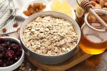 Making granola. Oat flakes in bowl, dried fruits and honey on wooden table, closeup