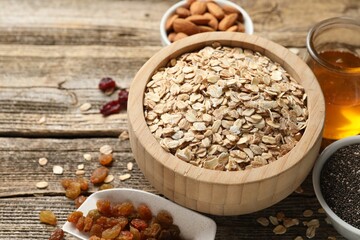 Making granola. Oat flakes in bowl, dried fruits, chia seeds, almond nuts and honey on wooden table, closeup