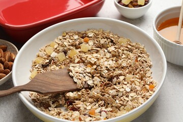 Making granola. Bowl of oat flakes, honey and dried fruits on light grey table, closeup