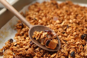 Tasty granola with dried fruits and spoon on tray, closeup