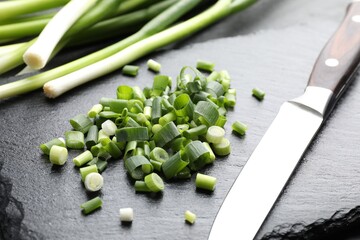 Whole, cut fresh green onions and knife on table, closeup