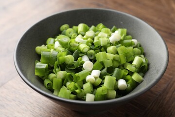 Cut green onion in bowl on wooden table, closeup