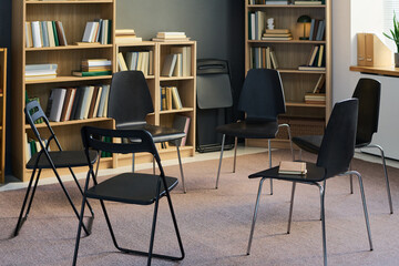 Empty chairs arranged in circle in therapy room suggesting group therapy session preparing for participants gathering, bookshelves filled with books in background
