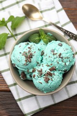 Tasty mint chocolate chip ice cream, spoon and towel on wooden table, top view