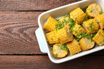 Pieces of boiled corncobs with green onion in baking dish on wooden table, top view. Space for text